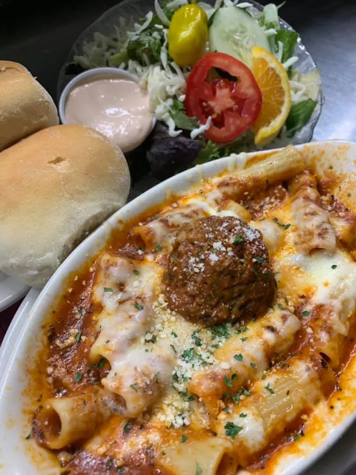 A plate of baked ziti and meatballs, served alongside a fresh salad and slices of bread from Tumea & Sons. The baked ziti is covered in melted cheese and tomato sauce, and the meatballs are generously portioned. The salad is fresh and colorful, with a mix of greens and vegetables, and the slices of bread are lightly toasted."