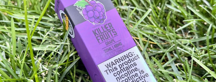 Featured image for the post, Vapetasia's Grape Nicotine Salt Review: These Killer Fruits are Tasty AF!" with the product box against a grass background.