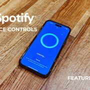 Smartphone displaying Spotify AI DJ voice command interface on a wood floor, with text overlay reading “Spotify AI DJ Voice Controls” and “Feature Review