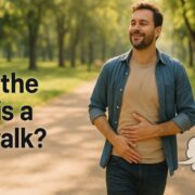 A smiling man walking through a sunlit park with one hand on his stomach, text on image reads “What the heck is a fart walk?”, with a cartoon fart cloud for humorous effect.