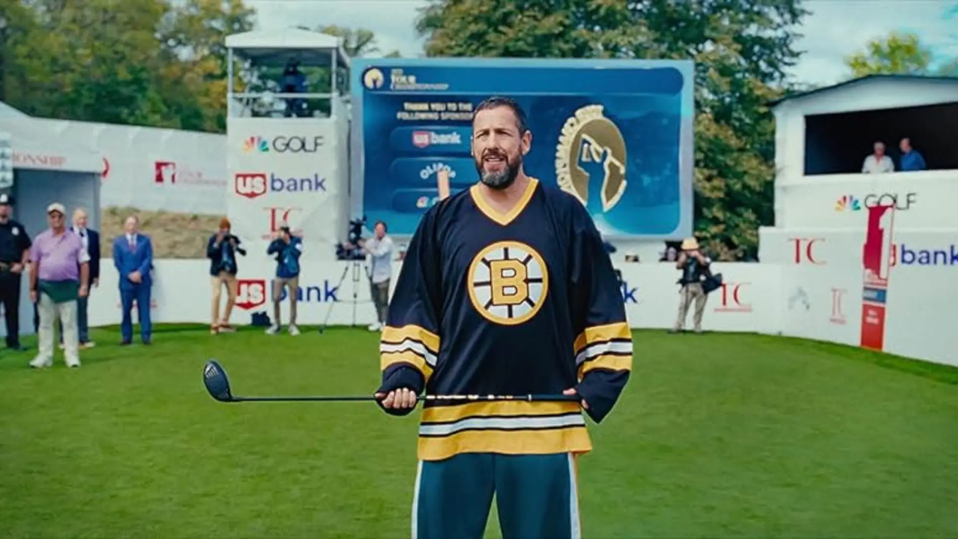 Adam Sandler as Happy Gilmore in the happy gilmore 2 trailer on a golf course wearing a Bruins jersey