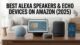 A collection of Amazon Echo devices on a wooden desk, including an Echo Show 15 smart display, Echo Studio speaker, a spherical Echo, and an Echo Dot, next to a smartphone running the Alexa app. The text overlay reads 'BEST ALEXA SPEAKERS & ECHO DEVICES ON AMAZON (2025)'.