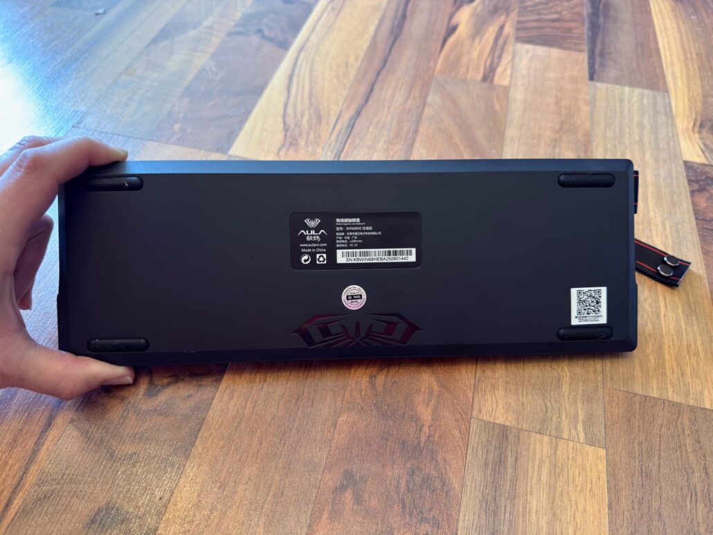 The underside of the black AULA WIN68 HE keyboard, showing the rubber feet, serial number, and product label.