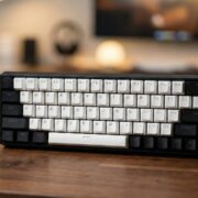 AULA WIN68 HE with Magnetic Switches A professional shot of the AULA WIN68 HE mechanical gaming keyboard sitting on a wooden desk, featuring black and white keycaps and a distinctive 'WING HE Series' carrying strap.