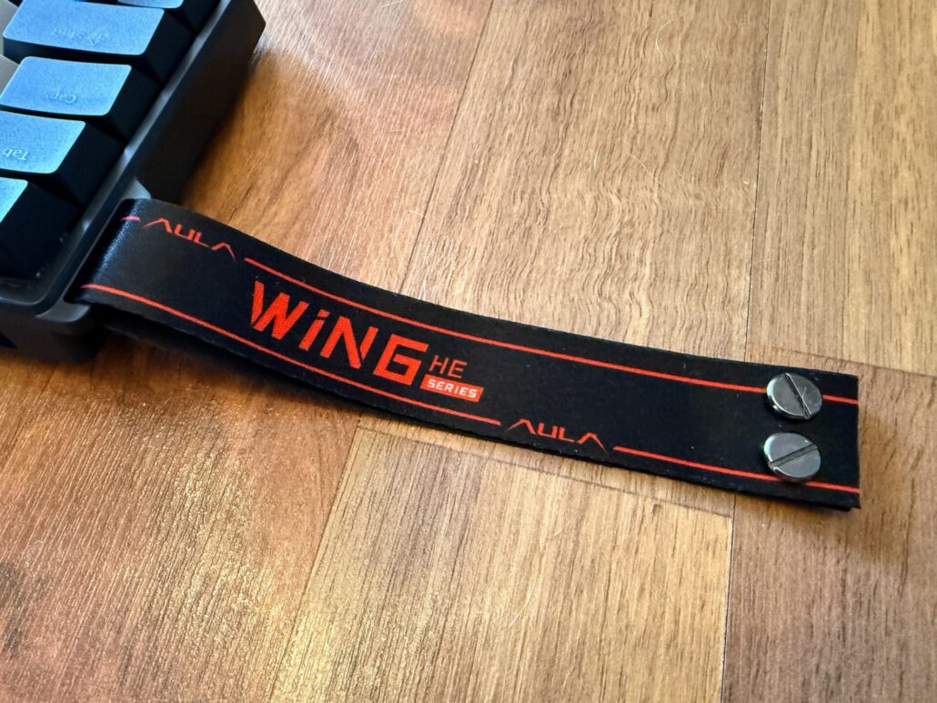 Close-up of the red and black AULA "WING HE Series" fabric carrying strap attached to the keyboard chassis.