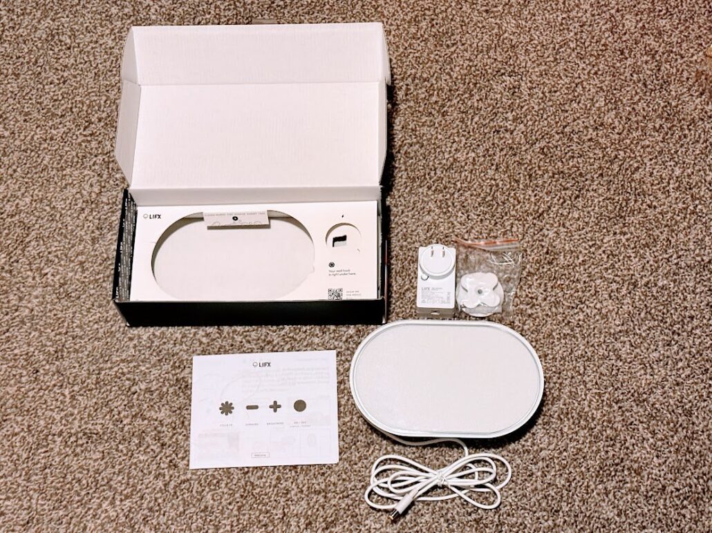 LIFX Luna smart lamp unboxed on a carpet beside its box, power supply, wall mount hardware, and quick start guide